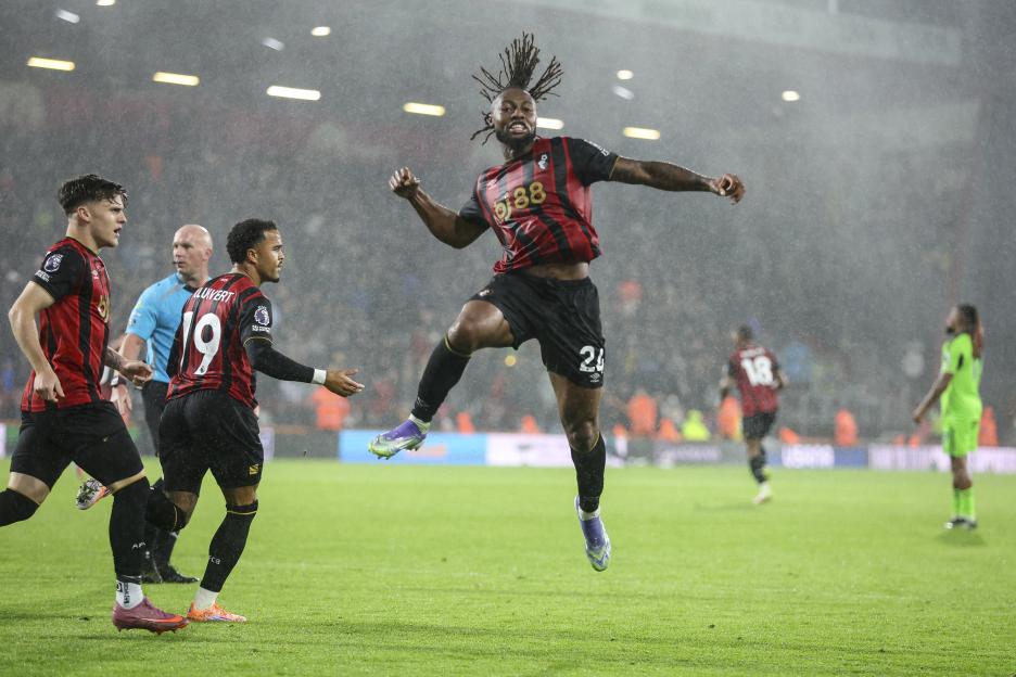Ghanaian striker Antoine Semenyo celebrates scoring a goal, with his right arm raised and left leg up, on a rainy night.