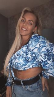 Woman smiling, wearing a blue and white patterned top and jeans.