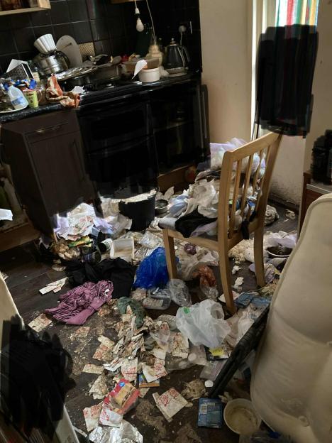 A very dirty kitchen with trash, clothes, and dishes scattered everywhere.