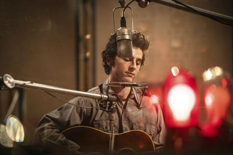 Timothée Chalamet playing guitar and harmonica in a recording studio.