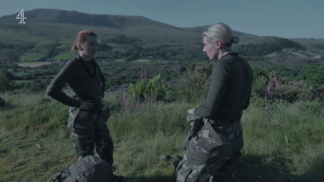 Two women in camouflage uniforms talking outdoors.