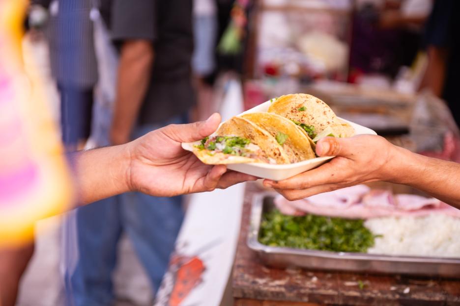 Tacos being handed to a customer at a Dia de los Muertos celebration.