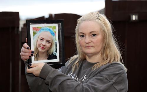 A mother holding a framed photo of her deceased daughter.