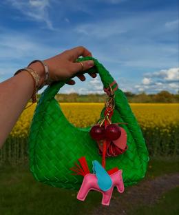 Woman holding a green woven handbag with a colorful key chain featuring cherries and a winged pony.