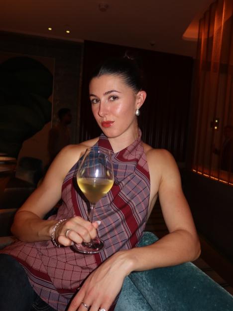 Amy Hunt holding a glass of white wine while sitting.