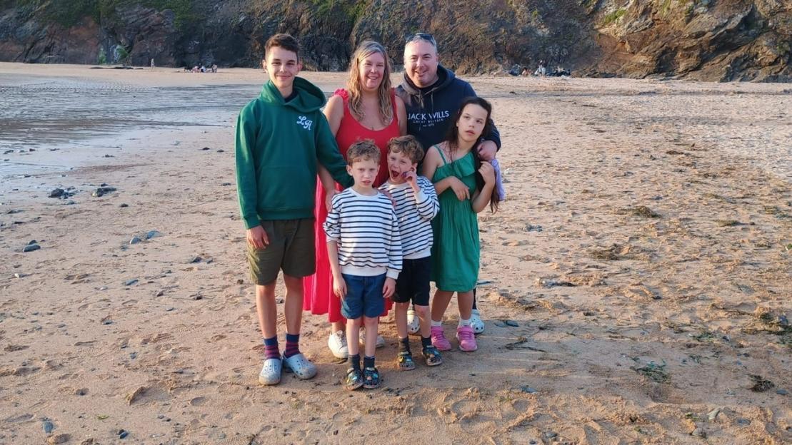 Kate Skelton and her husband Phil with their five children, including daughter Annabelle and twin boys Oliver and James, on a beach.