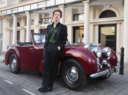 Damien Molony standing by a classic car at the Curzon Hoxton.