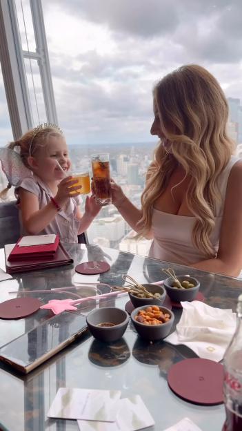 Stacey Solomon and her daughter, Rose, toasting drinks at a restaurant with a city view.