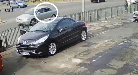 CCTV image of a silver car driving past a parked black car.