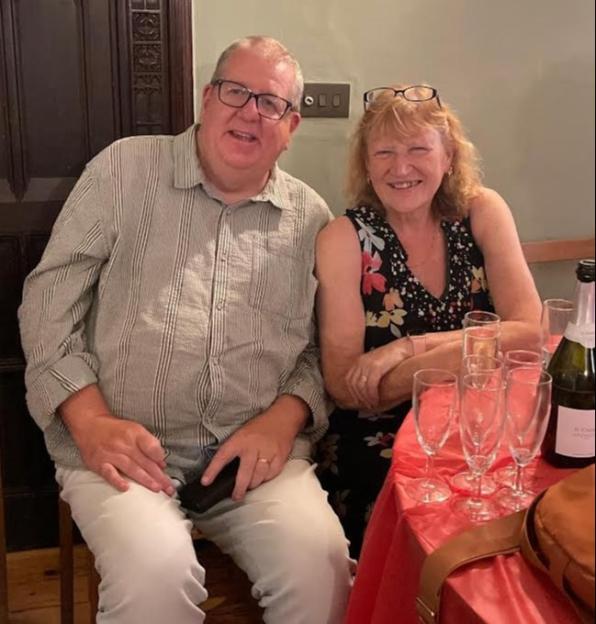 Man in striped shirt and woman in floral dress smiling at a table with champagne and glasses.