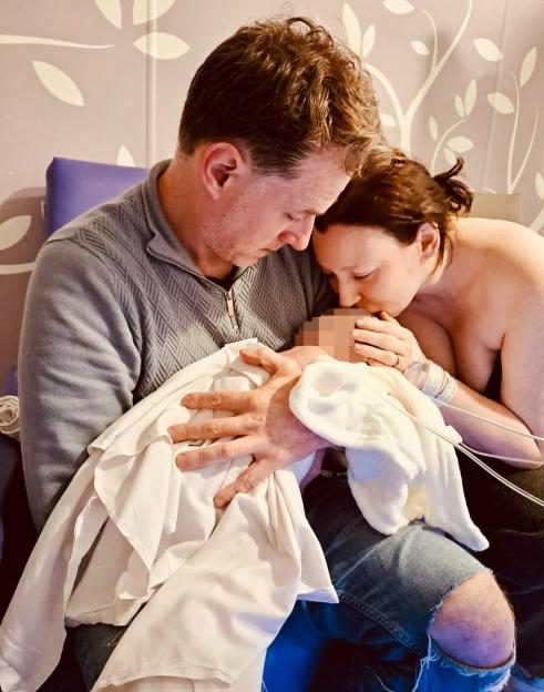Parents holding their newborn baby, with the mother kissing the baby's head.