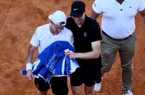 Jannik Sinner helping Jesper de Jong after a fall during a tennis match.
