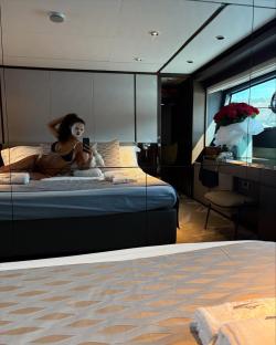 Maya Jama on a yacht, wearing a face mask and bikini, taking a selfie in a bedroom.