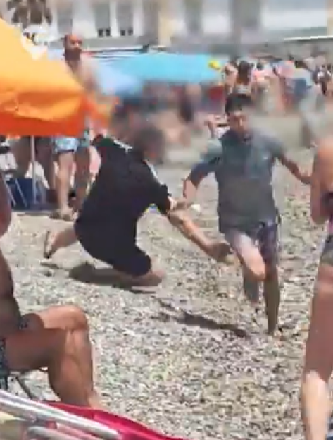 Two people grappling on a beach.