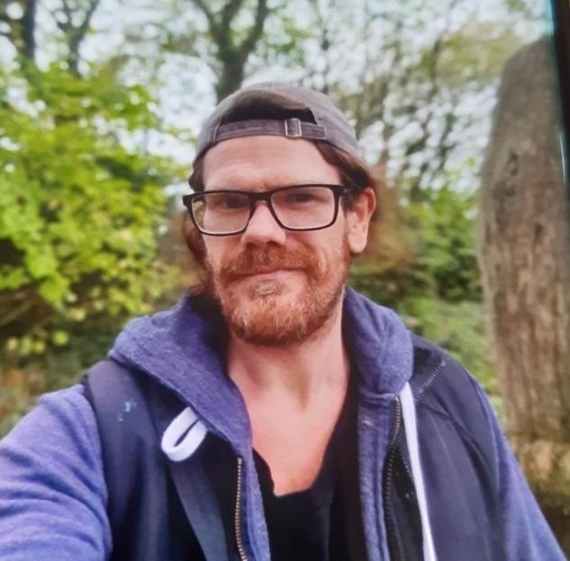Photo of a man with a beard and glasses wearing a baseball cap and purple jacket.