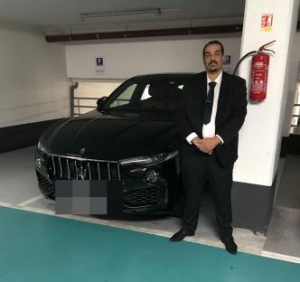 Taxi driver Nasim Mumin standing next to a black car in a parking garage.