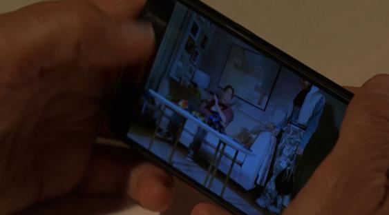 Person holding phone displaying video of two people in a living room.