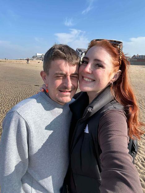 A man and a woman posing for a selfie on a beach.