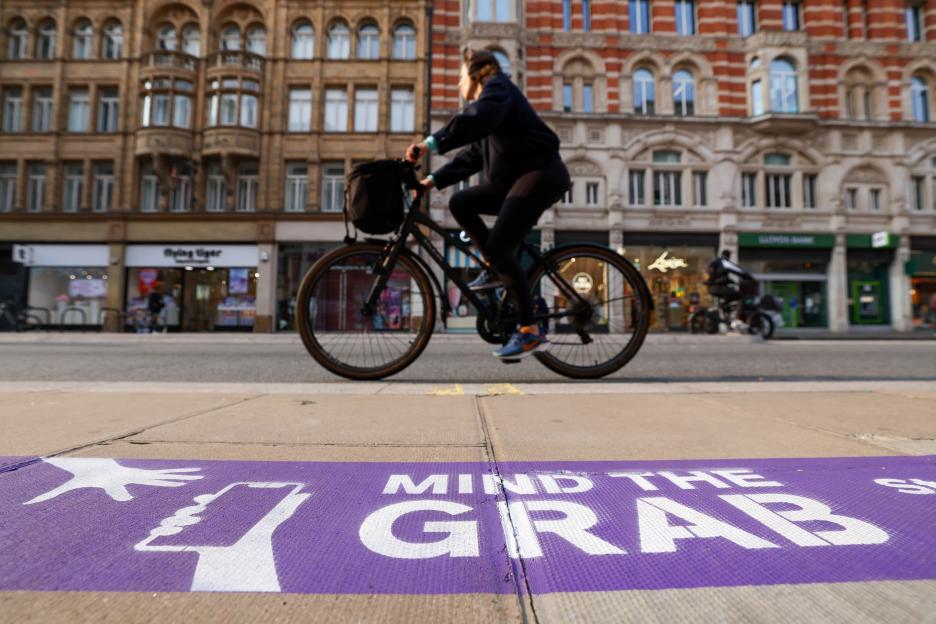 Purple pavement marking with "Mind the Grab" and a graphic of hands reaching for a phone.