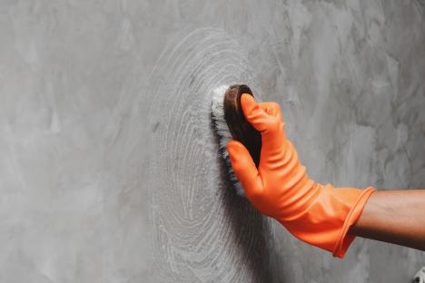 Hand in an orange glove scrubbing a concrete wall with a brush.