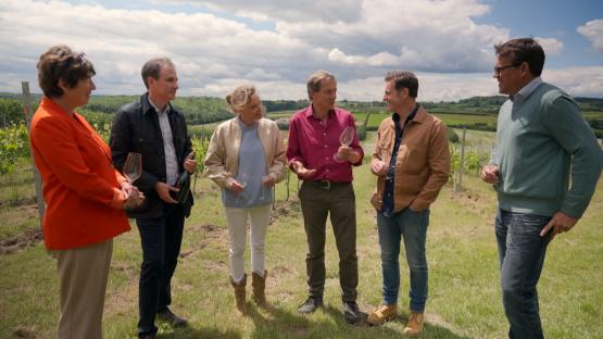 Matt Baker and a group of people stand in a vineyard, holding wine glasses.