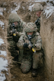 Three soldiers in camouflage uniforms crouched in a trench, aiming their rifles.