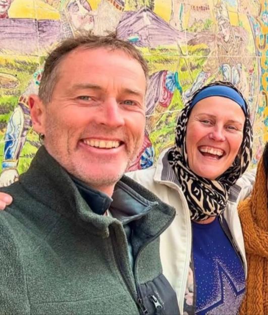 A man and woman smiling for a selfie in front of a colorful tiled wall.