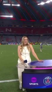 A woman stands at a TNT Sports desk on a soccer field.