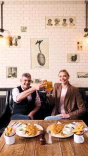 Two people toasting with beer in a pub.
