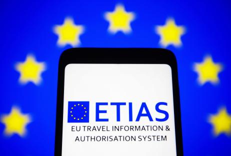 Smartphone displaying the ETIAS logo against a blurred EU flag background.