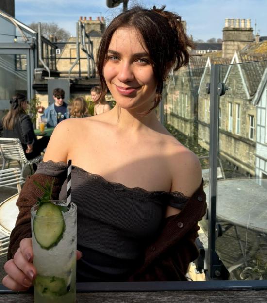 Woman holding a cucumber cocktail on a rooftop terrace.