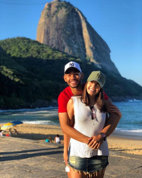 Couple embracing on beach with a large rock in the background.