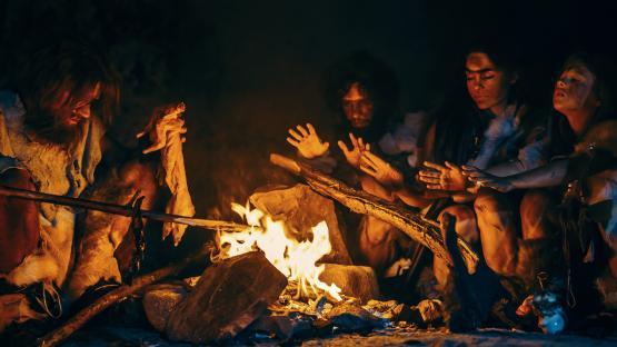 A Neanderthal or Homo Sapien family cooks and eats meat over a bonfire in a cave.