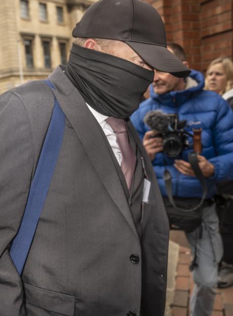 Robert Bush arrives at Hull Crown Court, wearing a black face covering, black baseball cap, gray suit, and light pink tie.