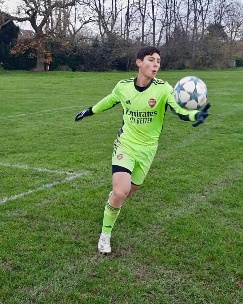 Soccer goalie in Arsenal gear making a save.