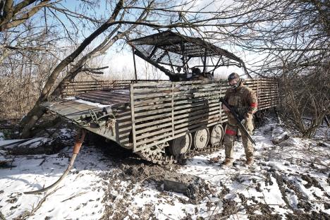 A soldier stands near a destroyed military vehicle.