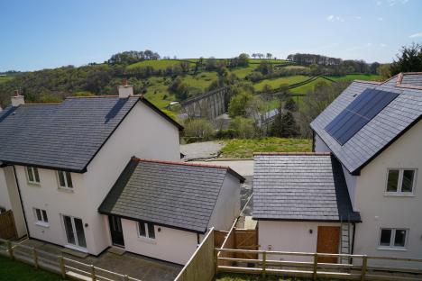 A deserted housing estate in Cornwall, UK, with boarded-up homes and a viaduct in the background.