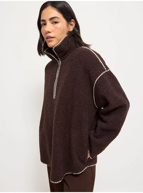 A person wearing a brown fleece half-zip sweatshirt with white blanket stitching.