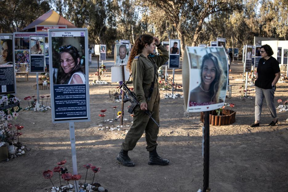 An Israeli army soldier with a rifle walks past memorials of victims from the 2023 October 7 attacks at the Nova Festival grounds.