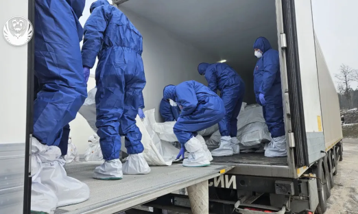 People in protective suits loading body bags into a truck.