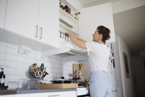 Woman reaching into a kitchen cupboard to get spices.