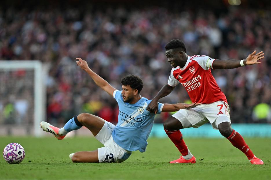 Matheus Nunes of Manchester City and Bukayo Saka of Arsenal vying for the ball during a football match.