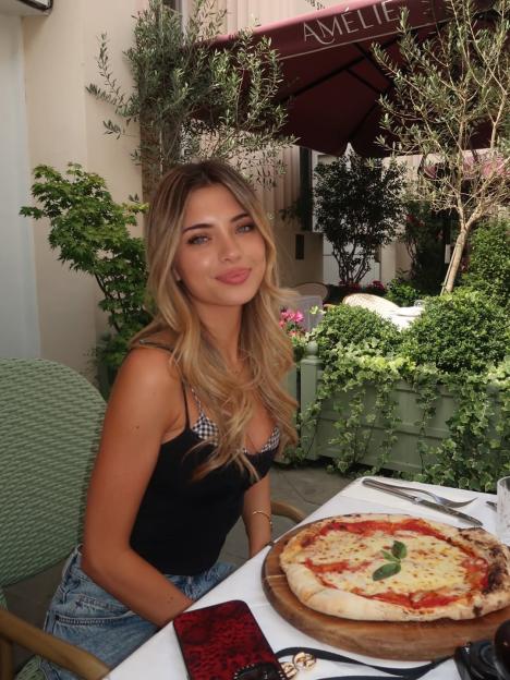 Talitha Balinska sitting at a restaurant table with a pizza.