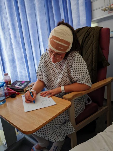 Woman in hospital gown drawing at a table.