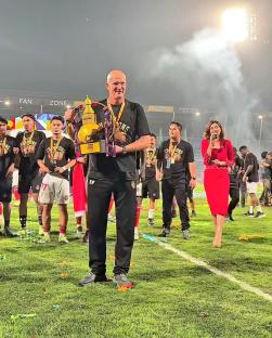 A soccer coach holding a trophy on a field with his team.