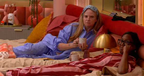 Two women in pajamas lying in bed, one holding a mug.