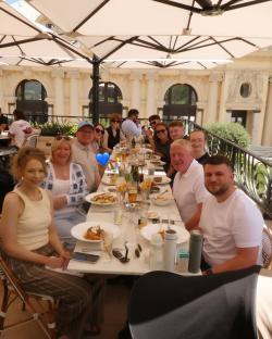Group of people sitting at a long table outdoors, enjoying a meal.