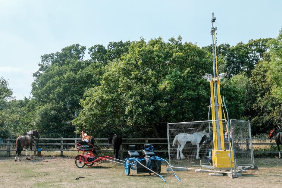 Horses and horse-drawn carriages near a tall camera system.
