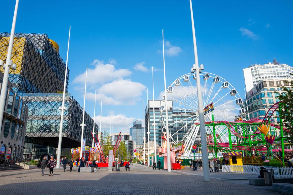 Amusement rides and Ferris wheel in a city square.