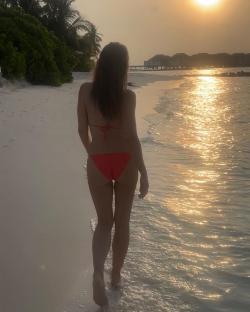 Woman in red bikini walking on beach at sunset.